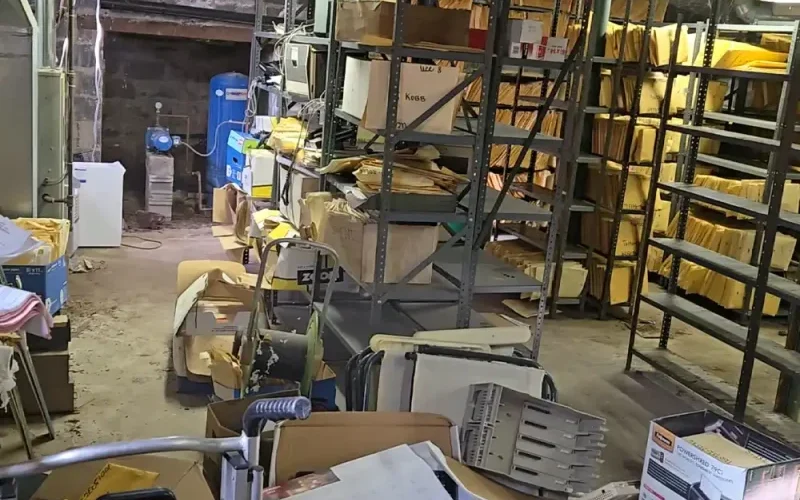 Cluttered commercial storage area with shelving, boxes and equipment ready for removal